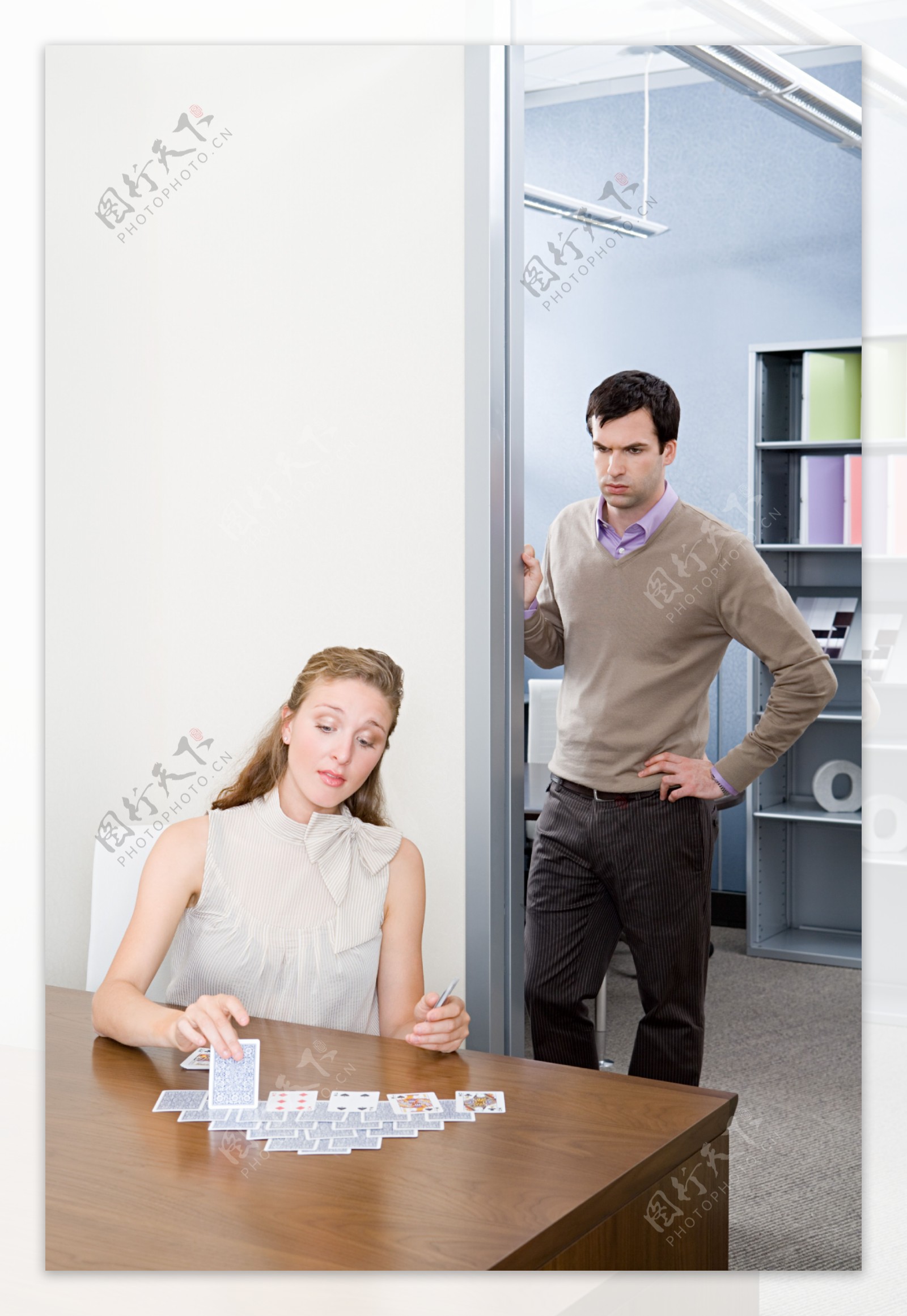 在办公室玩扑克牌的女人和倚在门边的男人图片
